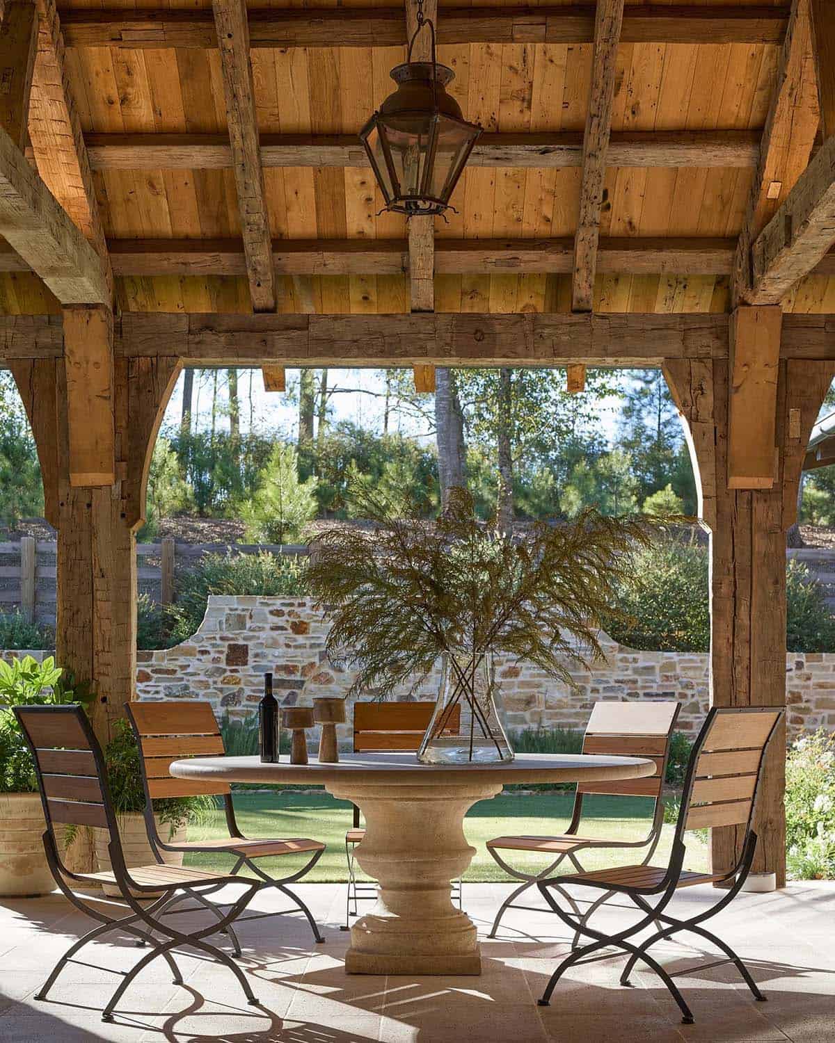 Covered outdoor dining pavilion with reclaimed timber beams, stone dining table, and garden views