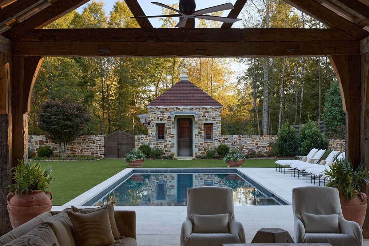 Pool pavilion view framing rectangular pool, stone pool house, and white lounge chairs at dusk