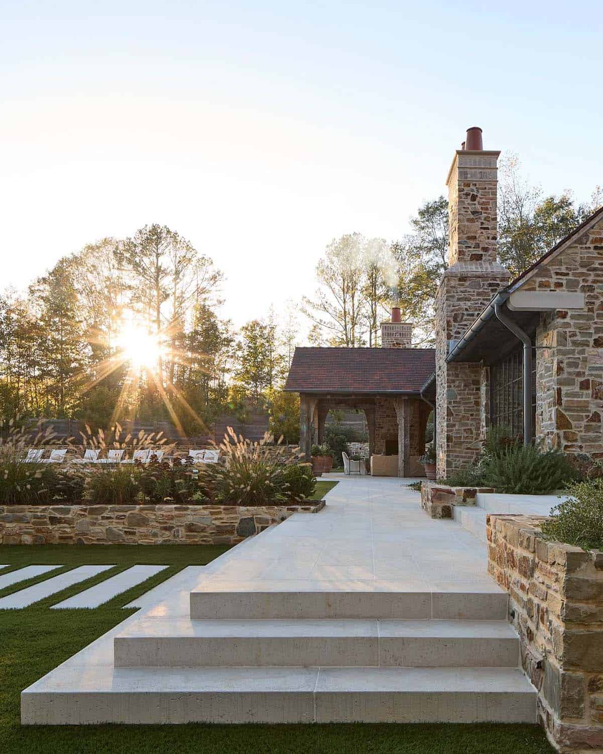 Stone home exterior at golden hour with limestone terrace, chimney, and timber pergola beyond