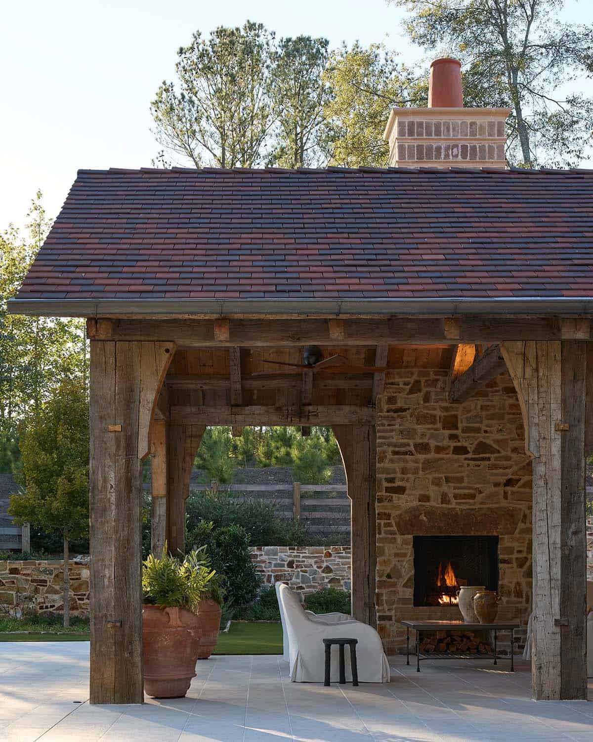 Outdoor covered pavilion with reclaimed timber frame, red tile roof, and stone fireplace