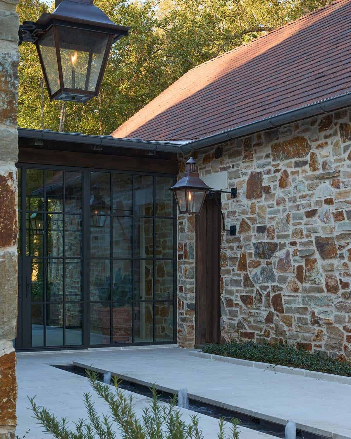 Stone home exterior detail with copper gas lanterns, steel-framed windows, and water feature