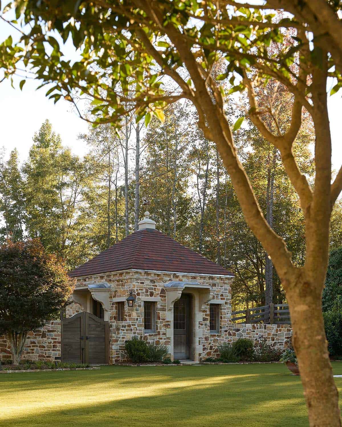 Stone pool house with red pyramid roof, arched doorway, and copper lantern among autumn trees