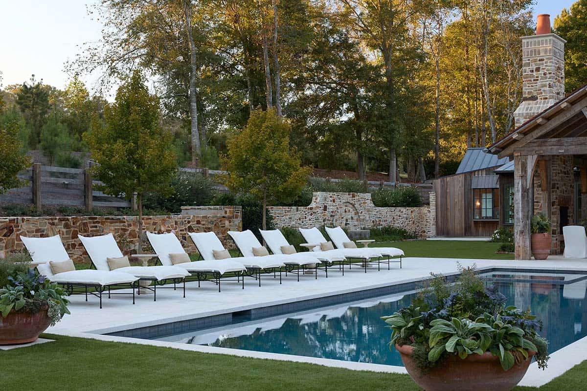 Rectangular pool with white lounge chairs, stone chimney, and reclaimed timber pavilion at dusk