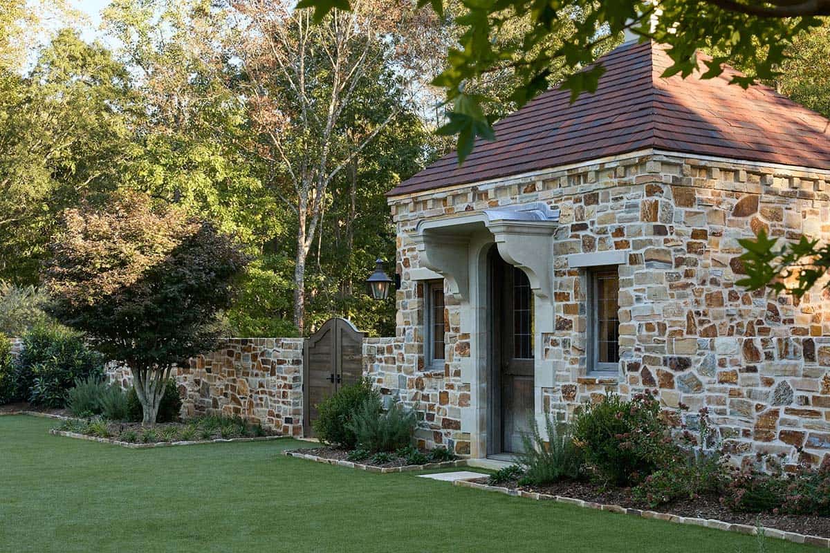 Stone pool house close-up with arched doorway, copper lantern, and manicured garden border