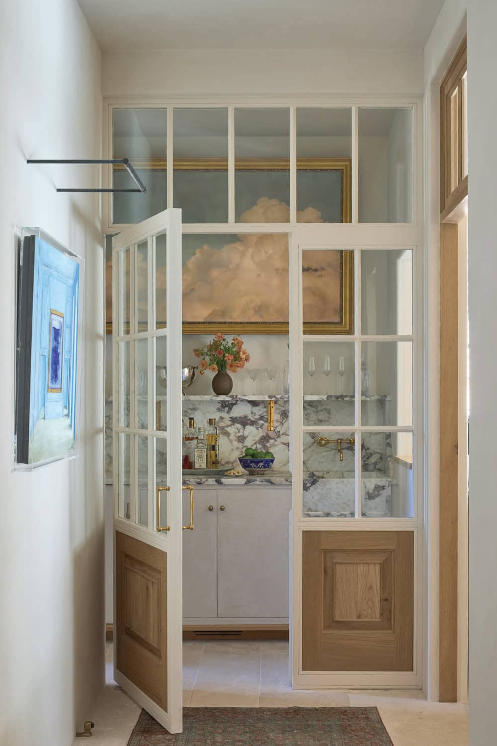 Butler's pantry bar seen through glass-paned doors with marble backsplash, cloud mural, and brass fixtures