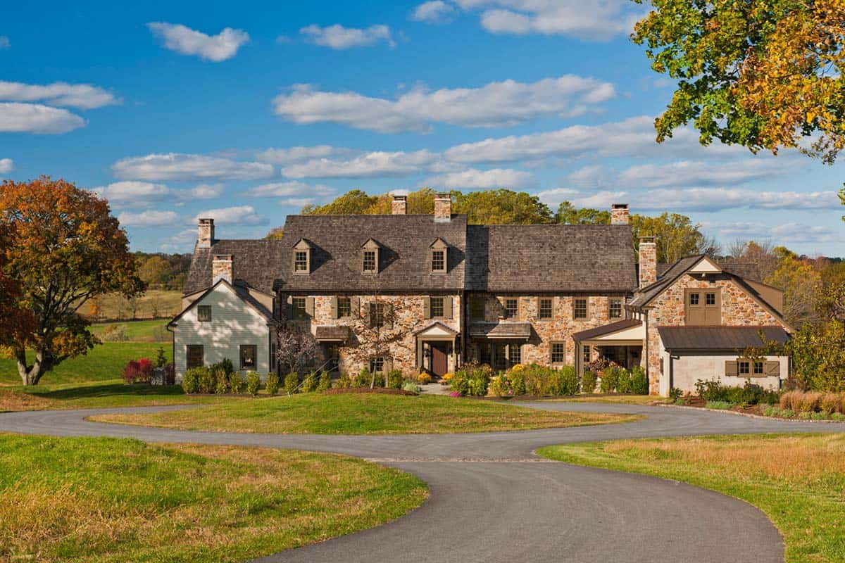 Large fieldstone farmhouse with multiple chimneys and dormers surrounded by foliage
