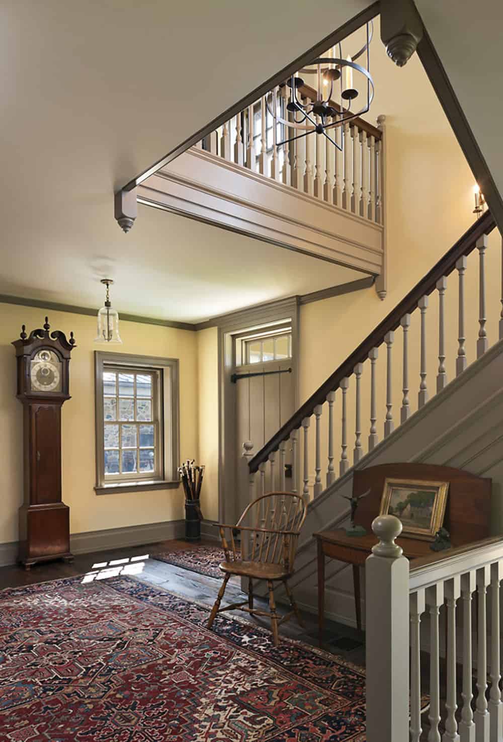 Colonial-style entry hall with painted staircase, wide-plank floors, and grandfather clock