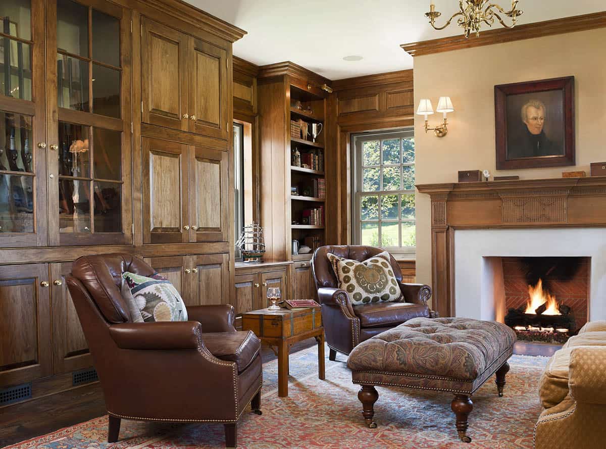 Wood-paneled study with leather armchairs, built-in cabinetry, and lit fireplace