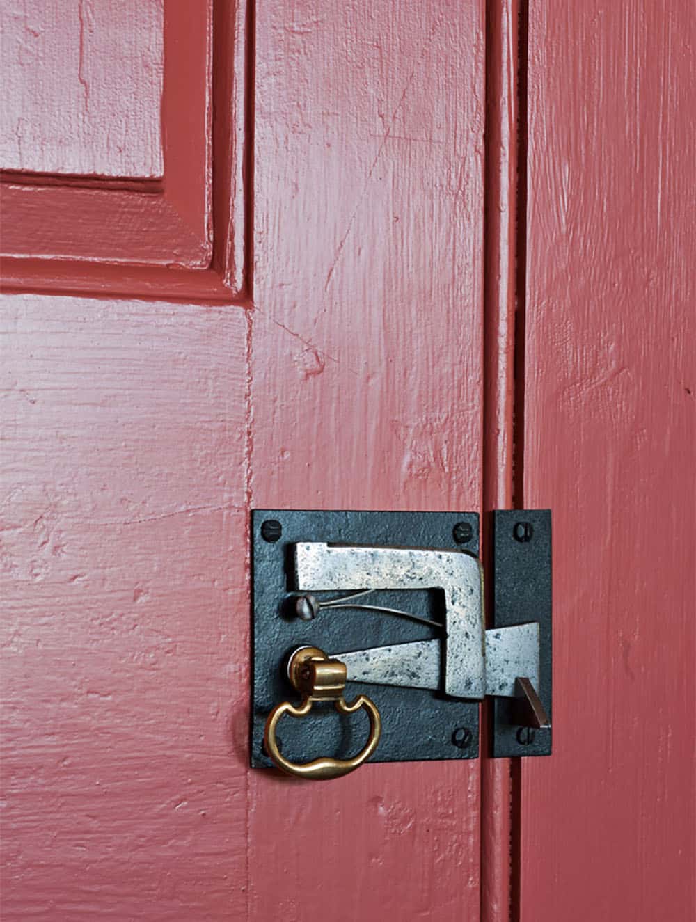 Close-up of antique iron door latch with brass ring pull on red painted door