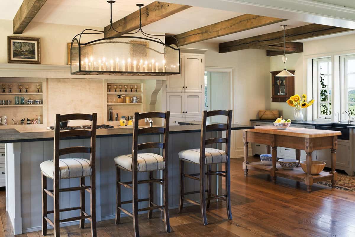 Farmhouse kitchen with exposed timber beams, gray island, ladder-back barstools, and iron candle chandelier