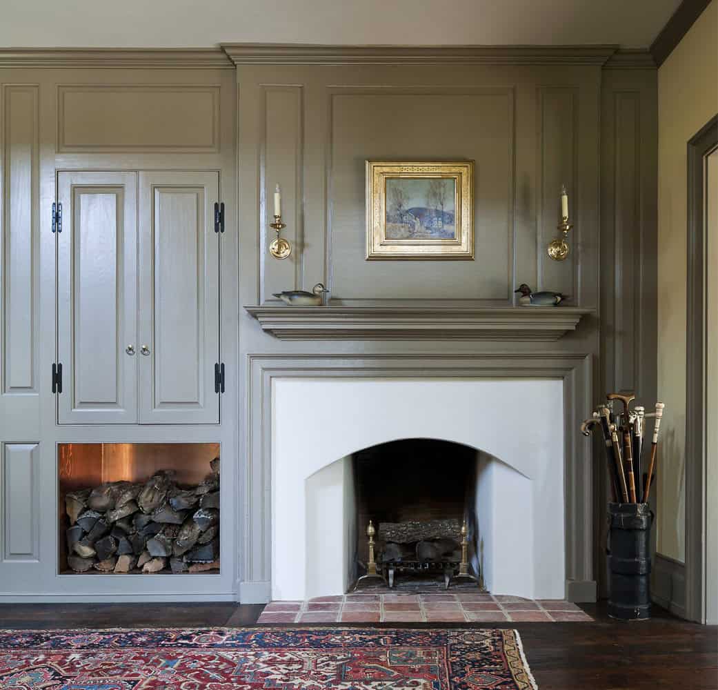 Colonial entry hall fireplace with gray painted paneling, built-in log storage, and duck decoys on mantel