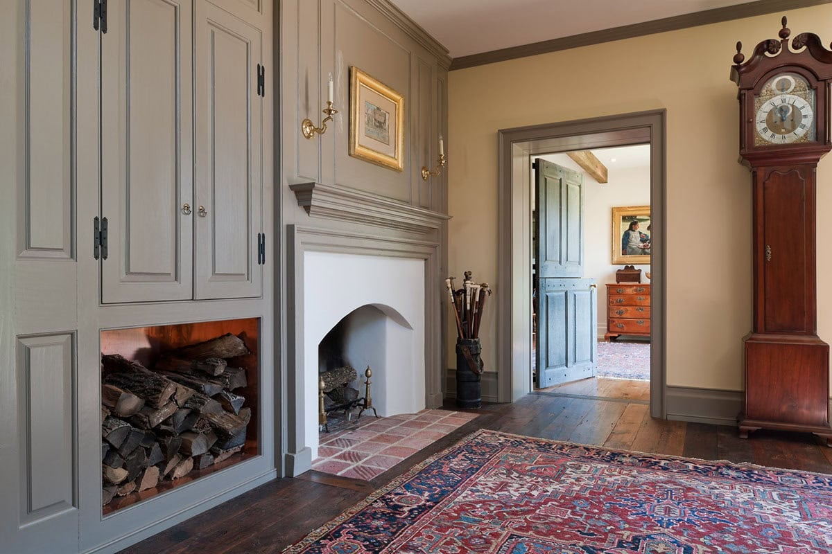 Gray painted entry hall fireplace with built-in cabinetry, grandfather clock, and view through to kitchen