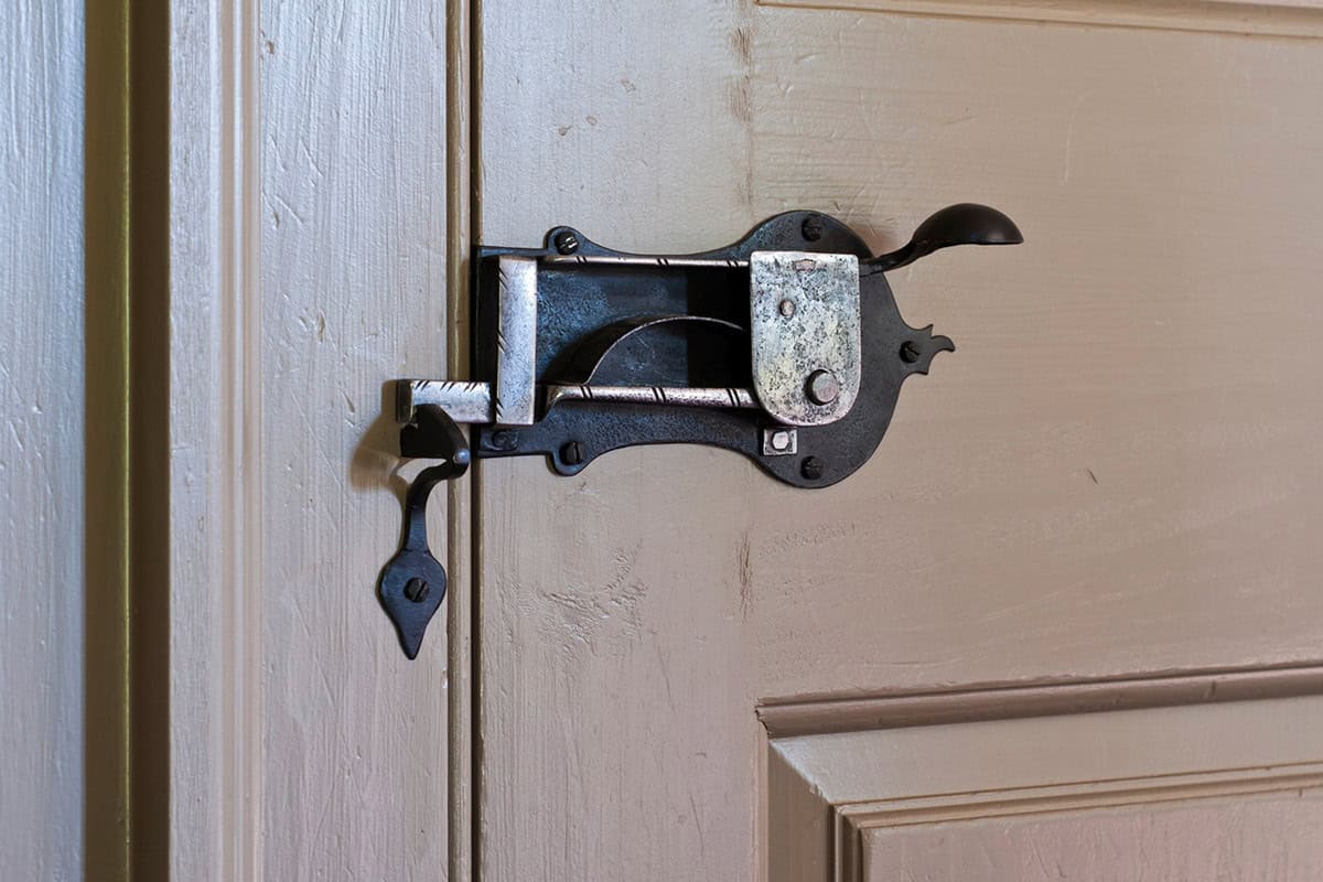 Close-up of ornate hand-forged iron door latch on painted cream-colored door