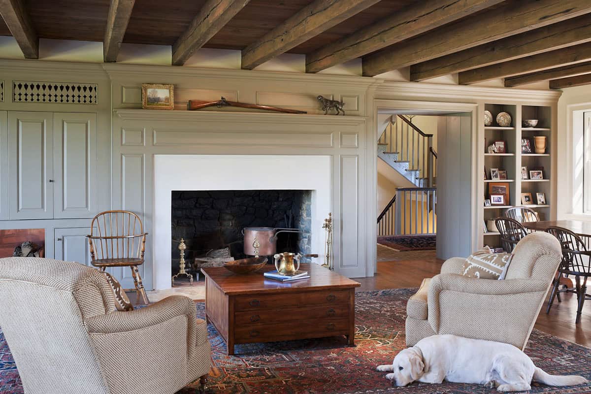Casual family room with exposed timber ceiling, sage painted paneling, stone fireplace, and yellow Labrador