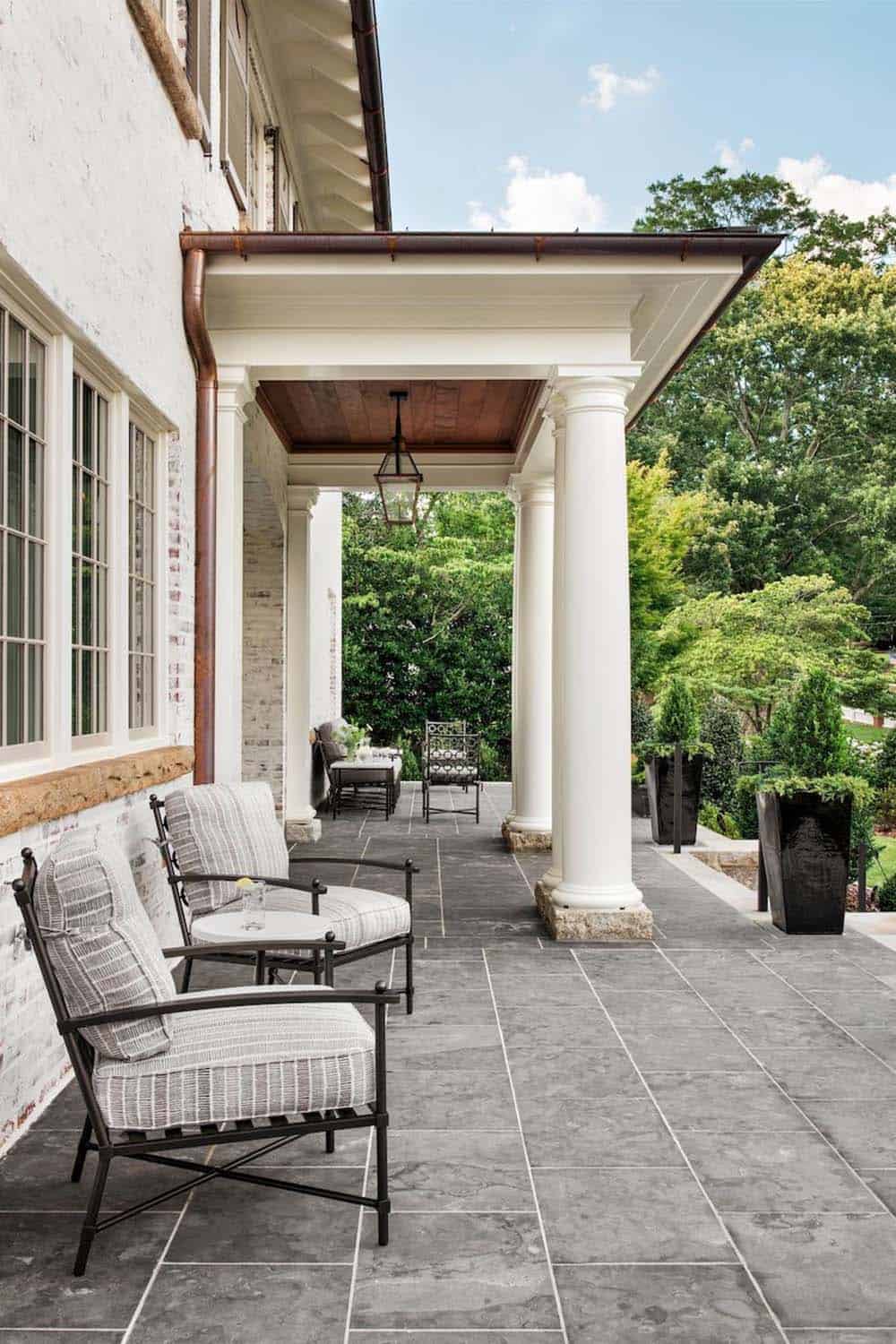 Columned back porch with gray stone tile flooring and wrought iron seating