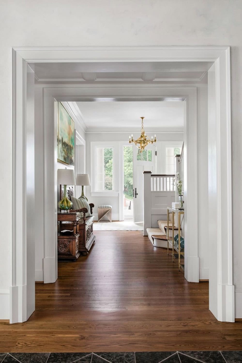 Hallway entry with wide white molded doorframe, hardwood floors, and brass chandelier