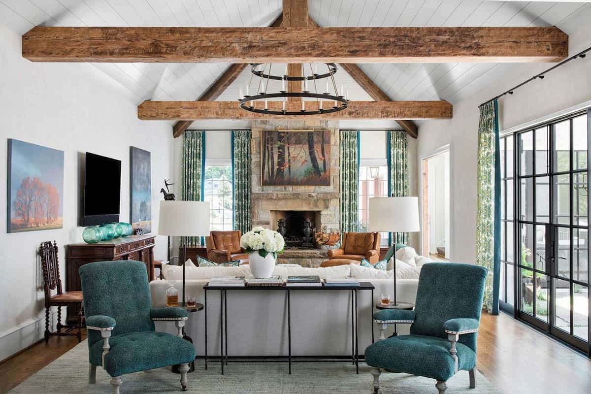 Great room with exposed wood beam vaulted ceiling, stone fireplace, and teal accent chairs
