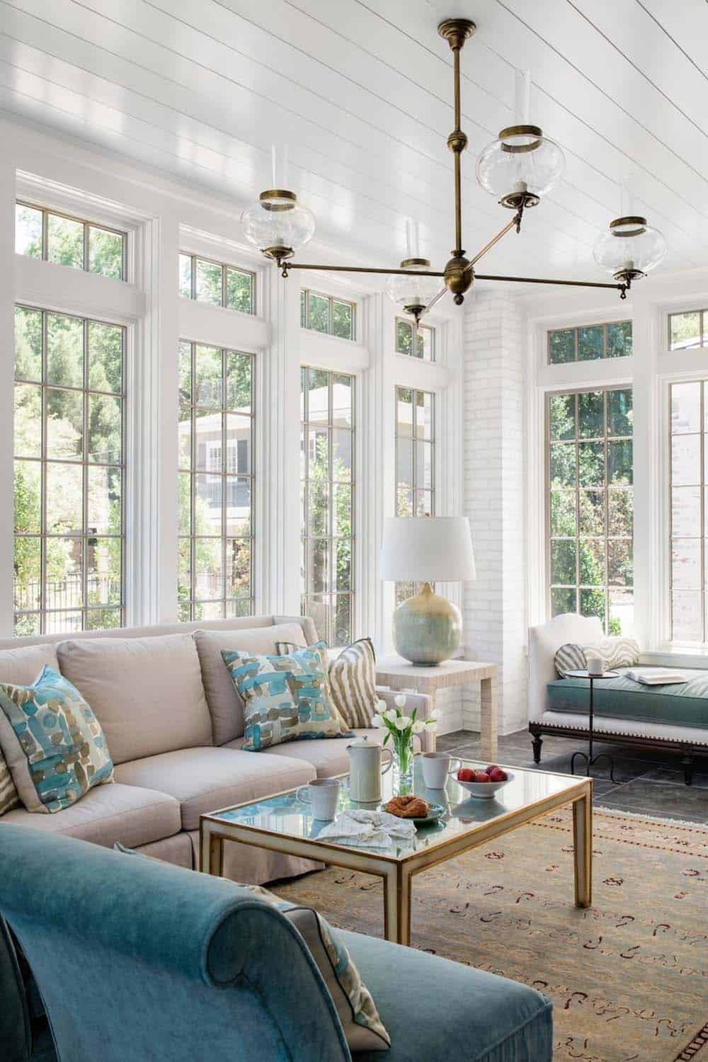 Bright sunroom with floor-to-ceiling white-framed windows and brass globe chandelier
