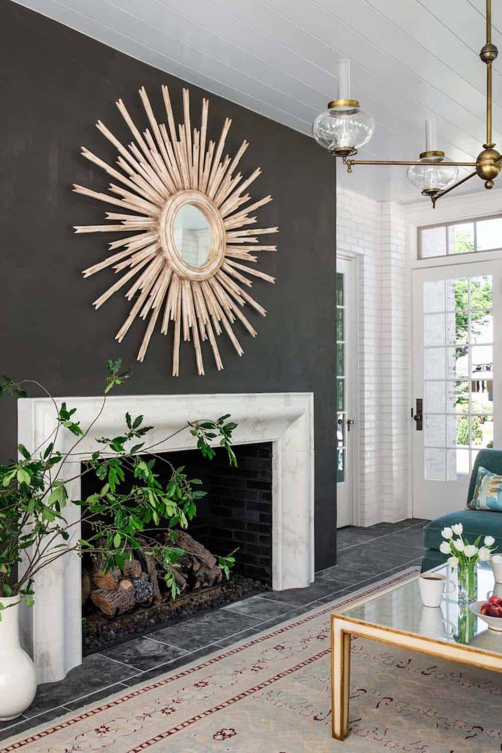 Sunroom fireplace with marble surround, dark accent wall, and large starburst mirror