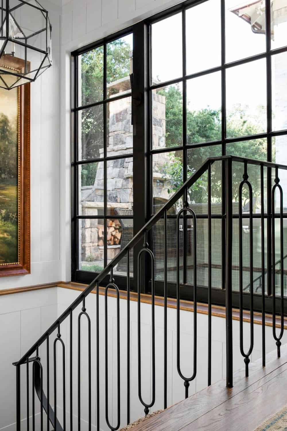 Staircase landing with black steel-framed windows overlooking stone outdoor fireplace