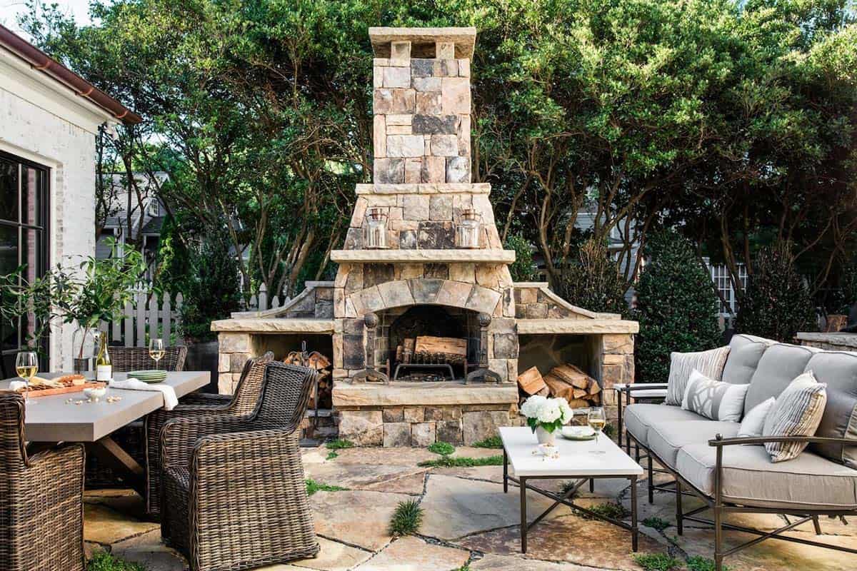 Stone outdoor fireplace with flagstone patio, wicker dining chairs, and upholstered seating