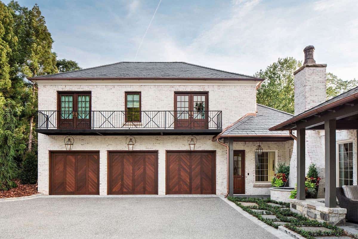 White painted brick carriage house with three wood chevron garage doors and upper balcony