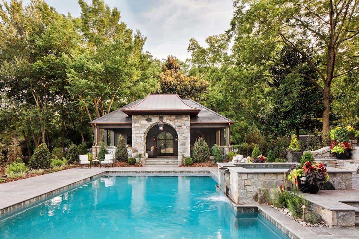 Rectangular swimming pool with stone pool house featuring arched entry and copper roof