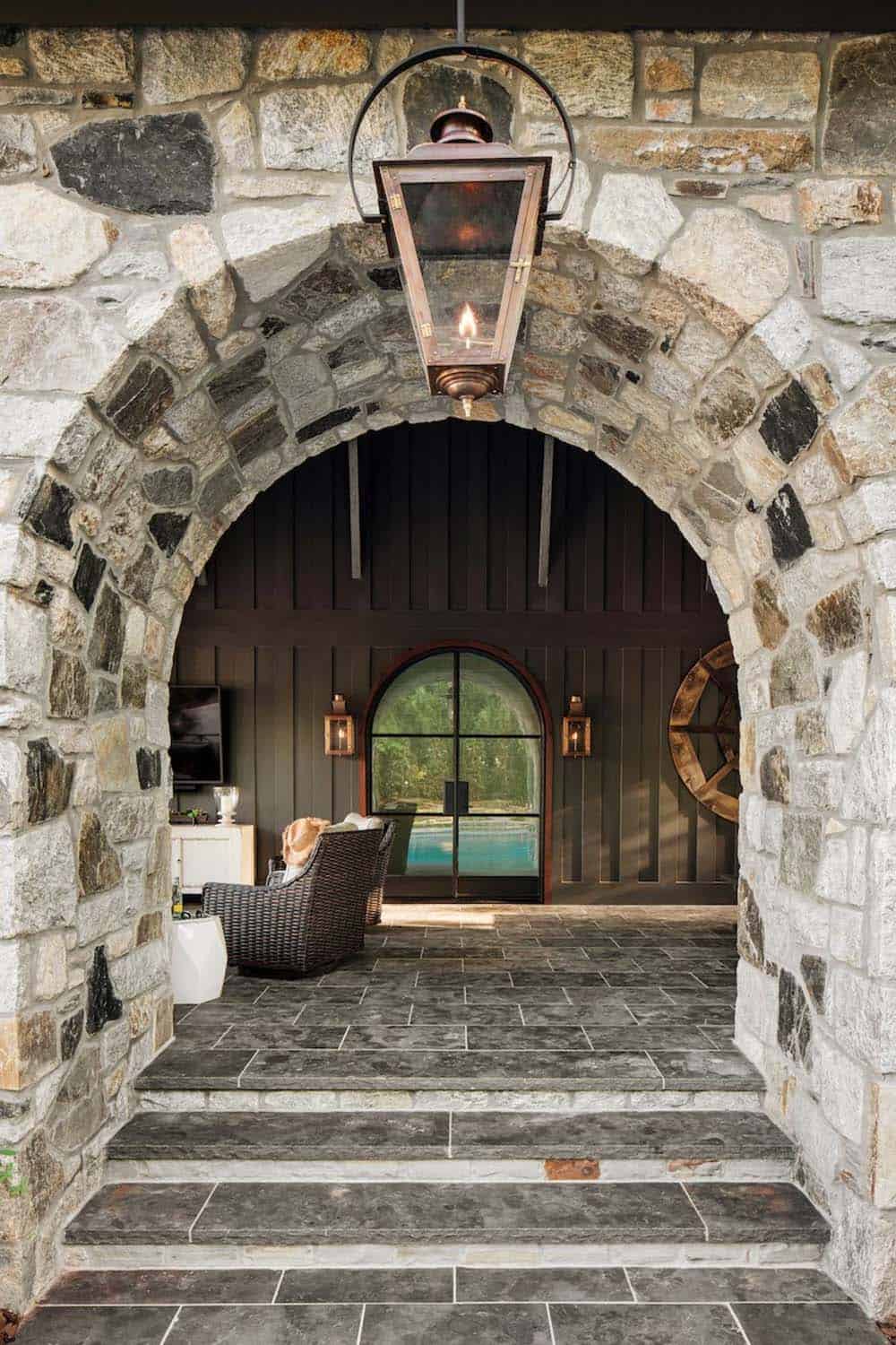 Stone arched pool house entrance with copper gas lantern and slate tile steps