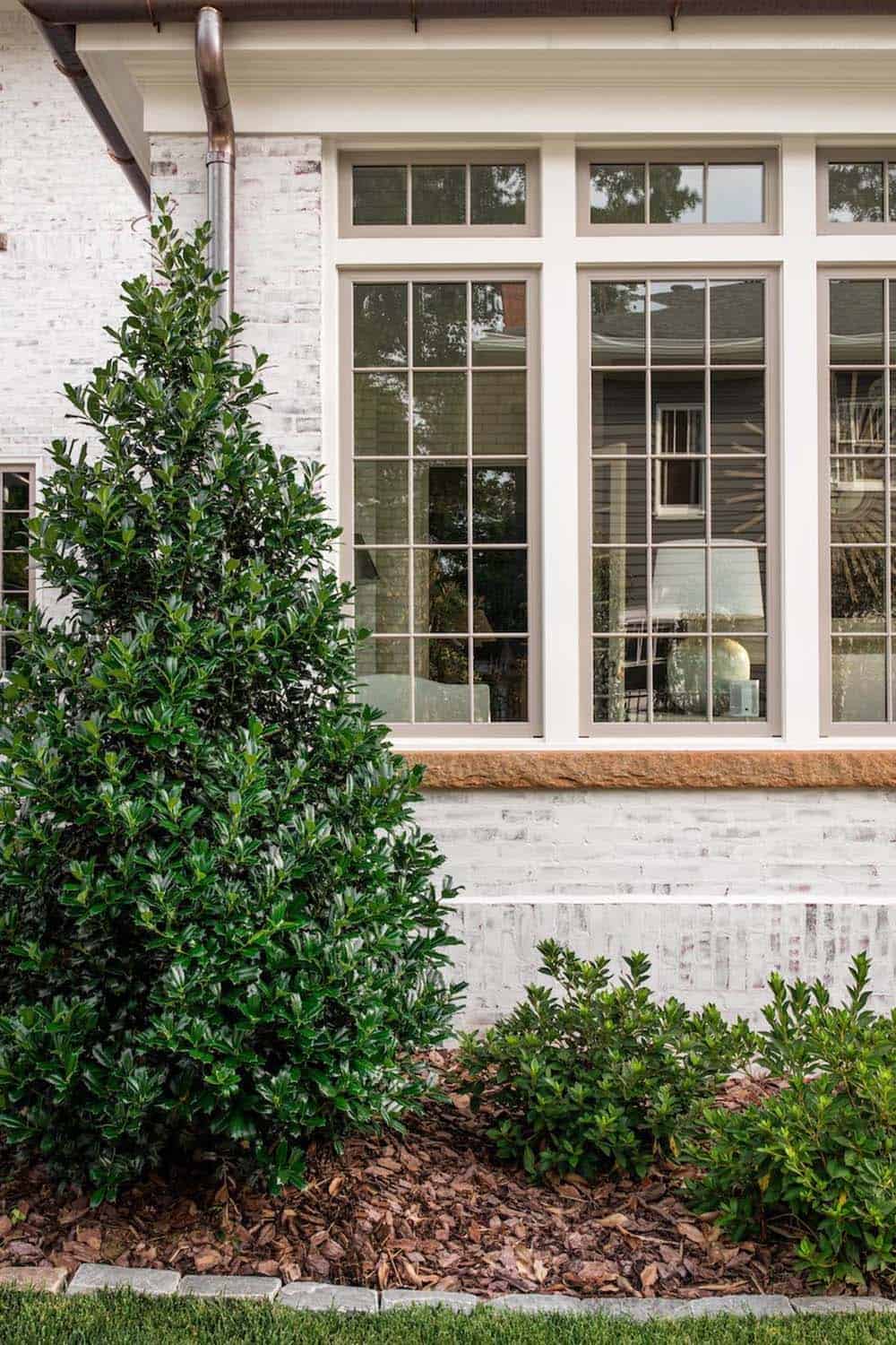 Close-up of white brick sunroom exterior with large grid windows and magnolia landscaping