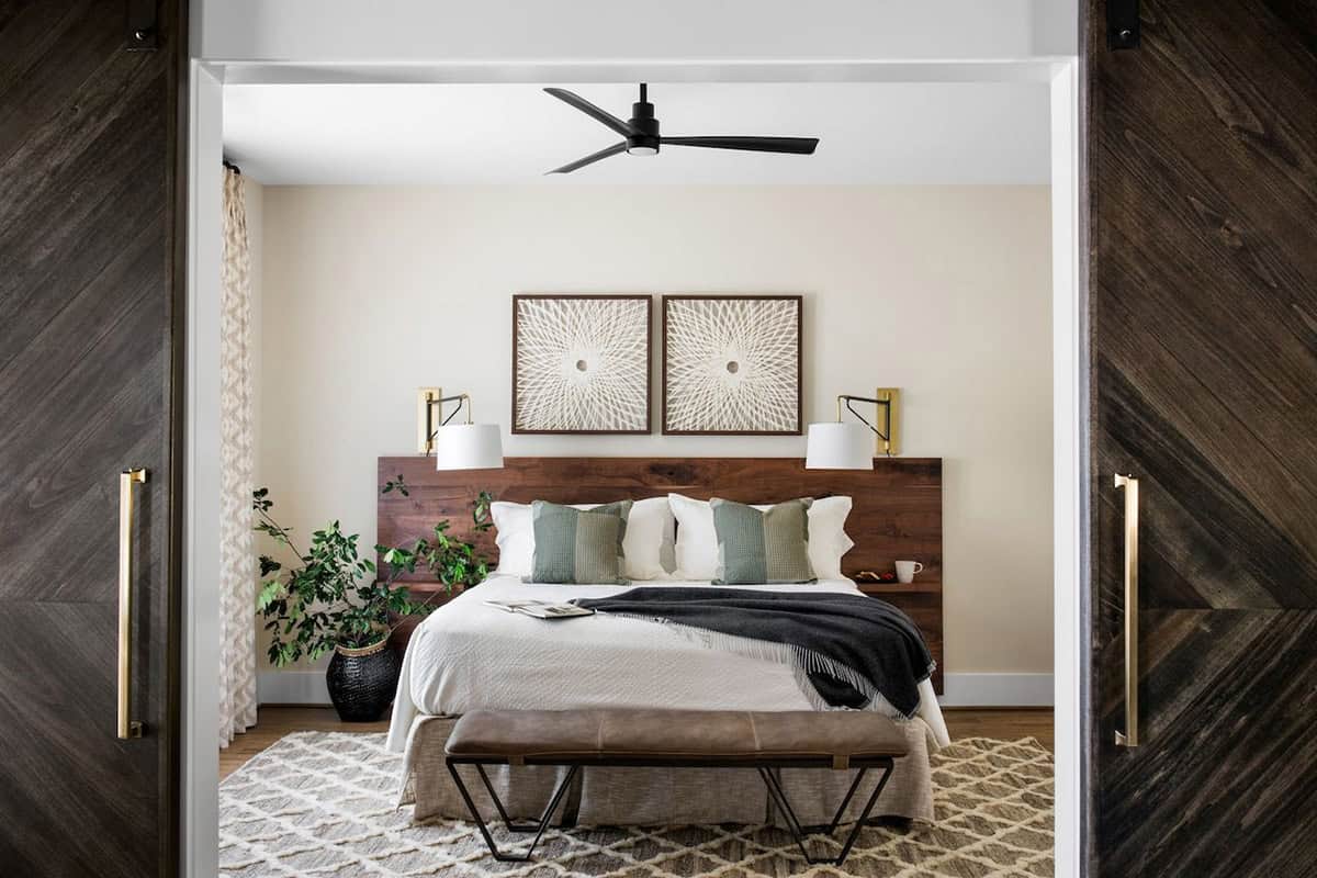 Pool house bedroom seen through dark wood barn doors with walnut headboard and neutral linens