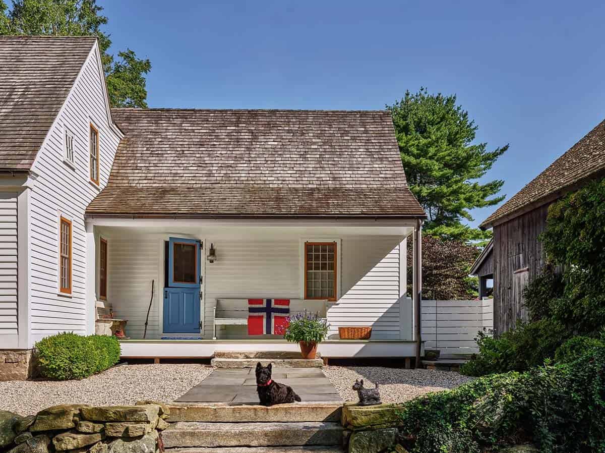 Covered back porch of white farmhouse with blue Dutch door, Norwegian flag, and two Scottish terriers