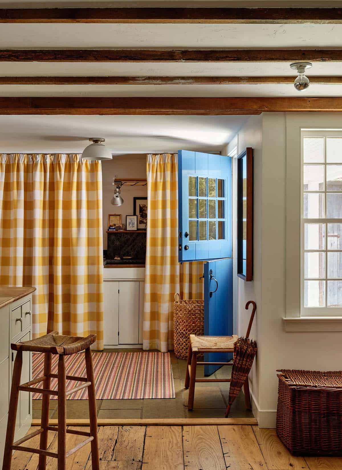 Farmhouse entryway with yellow gingham curtains, blue Dutch door, exposed beams, and rush-seat barstools