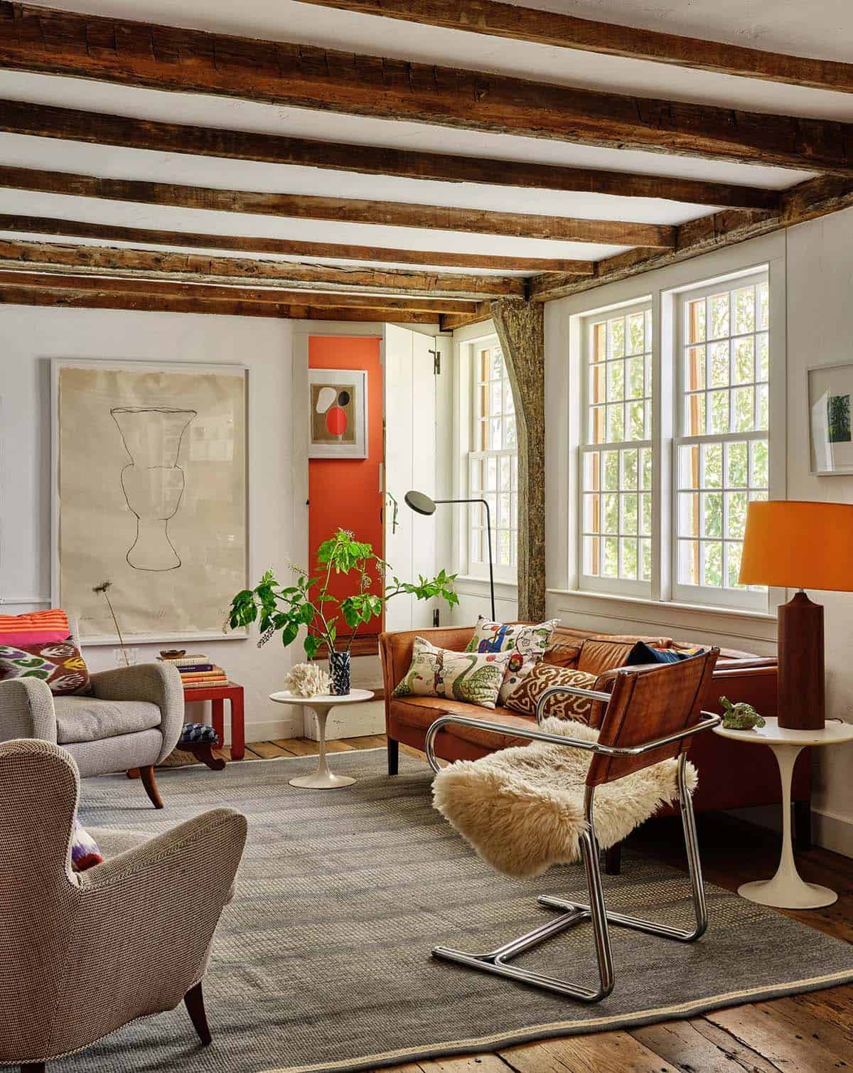 Eclectic living room with exposed timber beams, leather sofa, chrome cantilever chair, sheepskin throw, and large-scale wall art