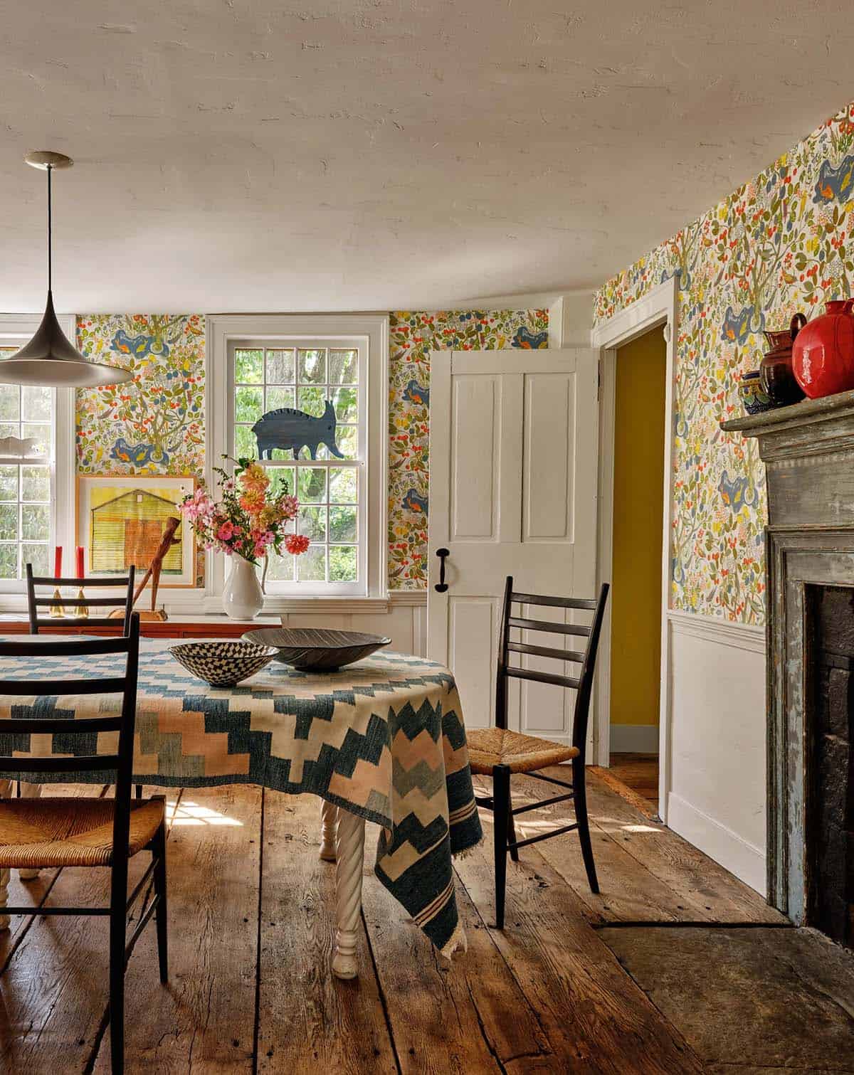 Dining room detail with vibrant folk-print wallpaper, original fireplace surround, and yellow-painted hallway beyond
