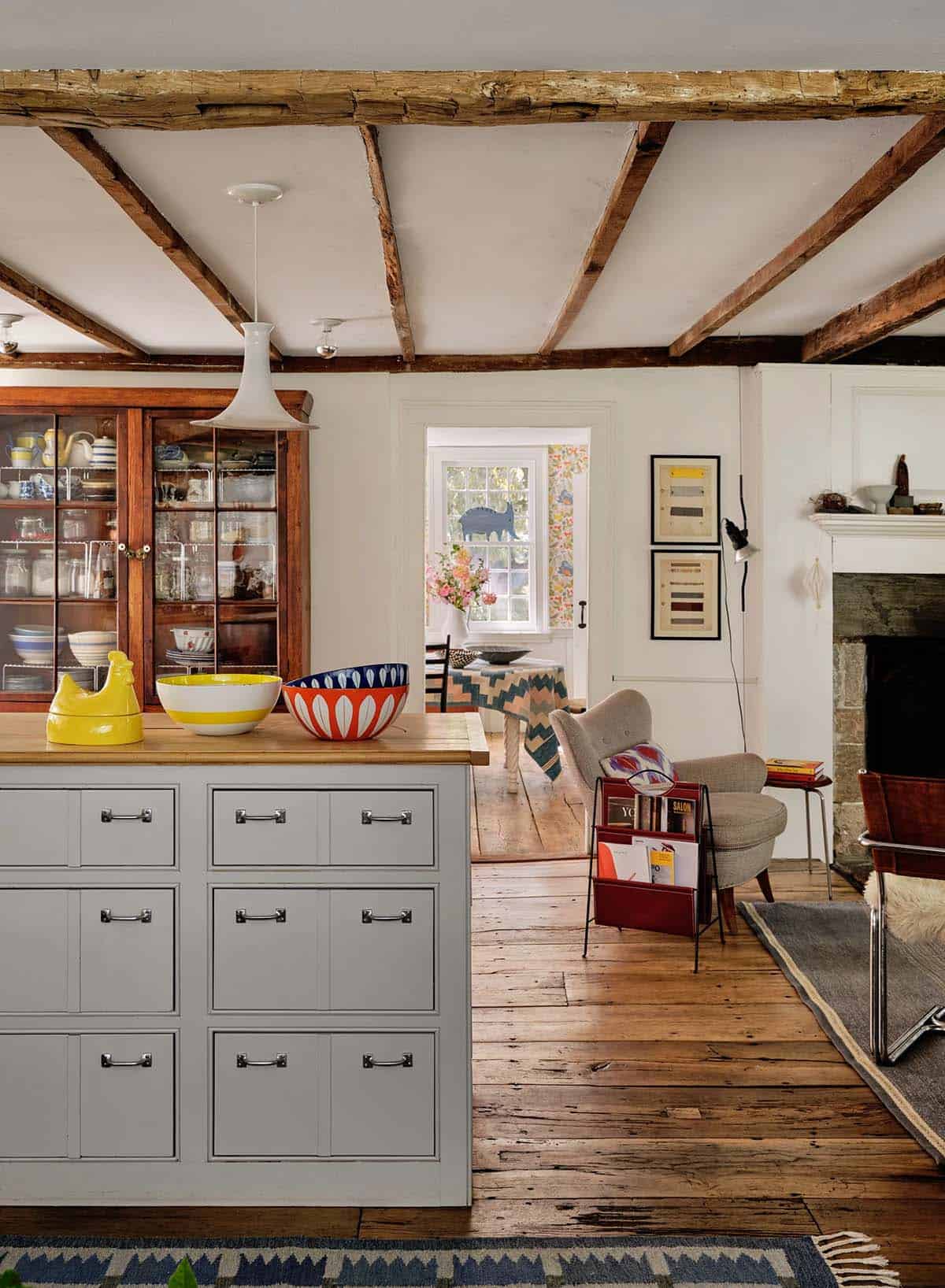 Open-plan kitchen and living area with gray island, antique hutch, exposed beams, and wide-plank floors