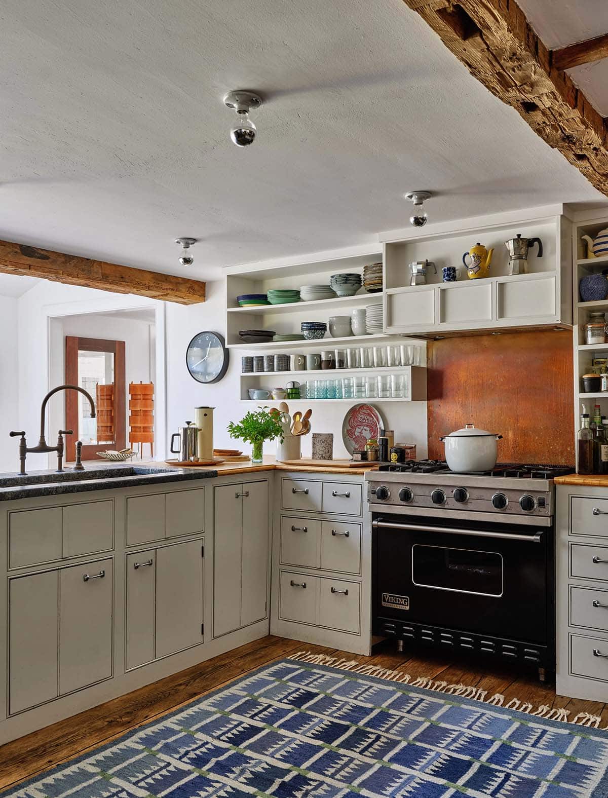 Farmhouse kitchen with sage green cabinets, copper backsplash, Viking range, open shelving, and bridge faucet