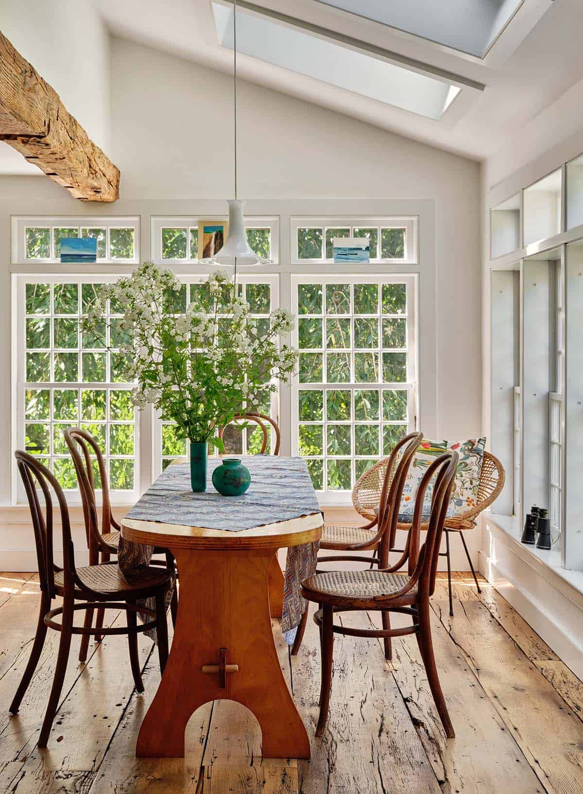 Bright breakfast room addition with tall gridded windows, skylight, wood trestle table, and bentwood chairs