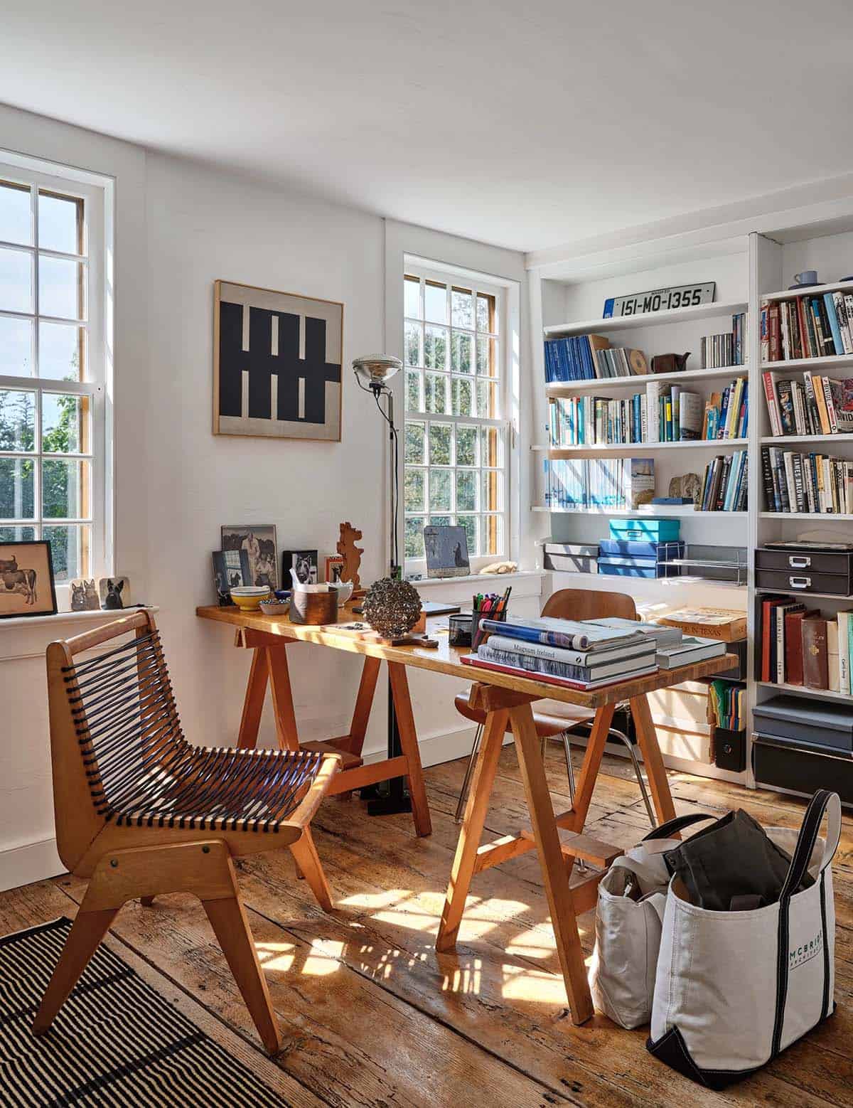 Sunlit home office with sawhorse desk, Pierre Jeanneret chair, built-in bookshelves, and wide-plank floors