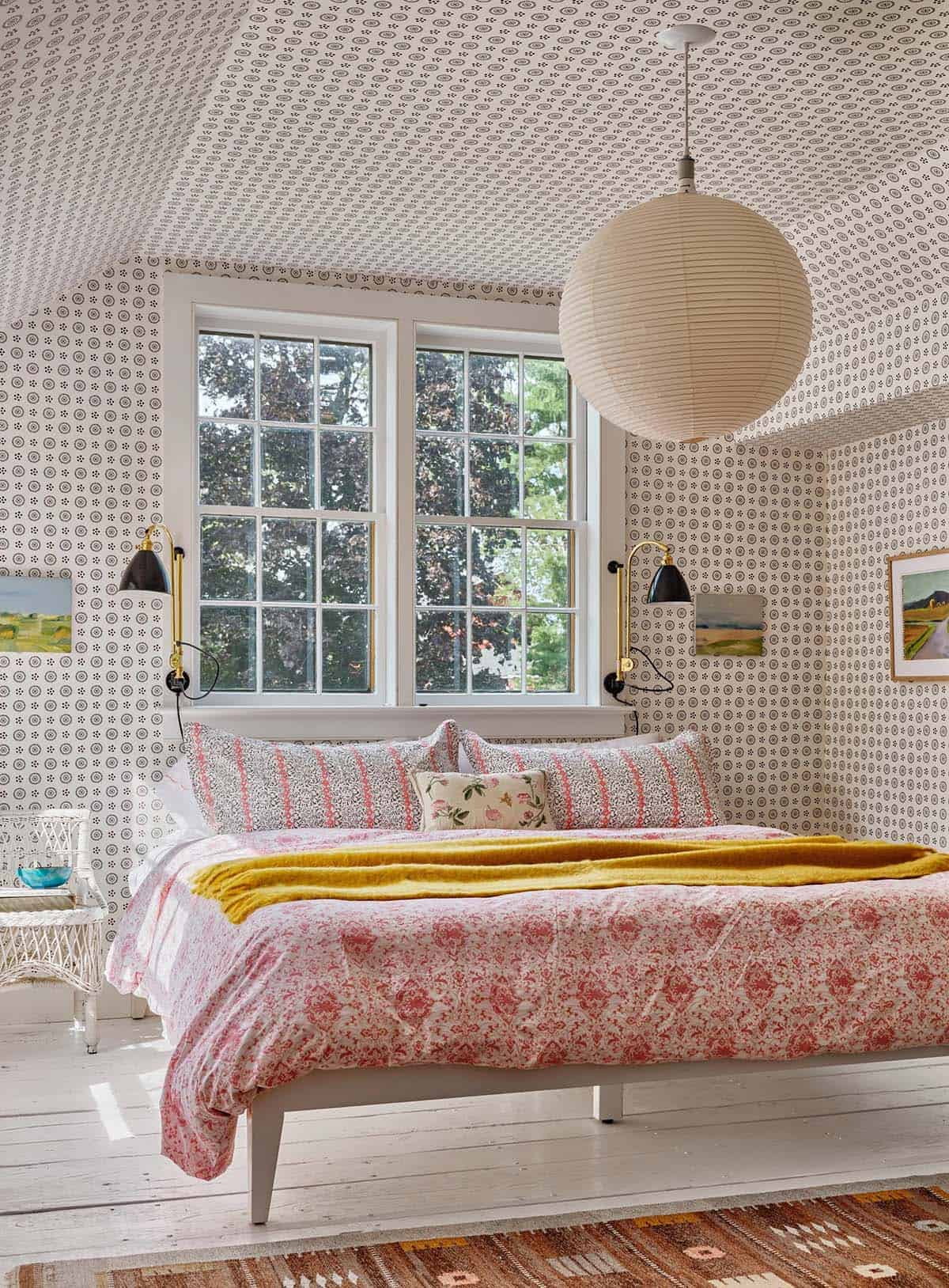 Attic bedroom with small-print wallpaper covering walls and ceiling, paper globe pendant, and pink floral bedding