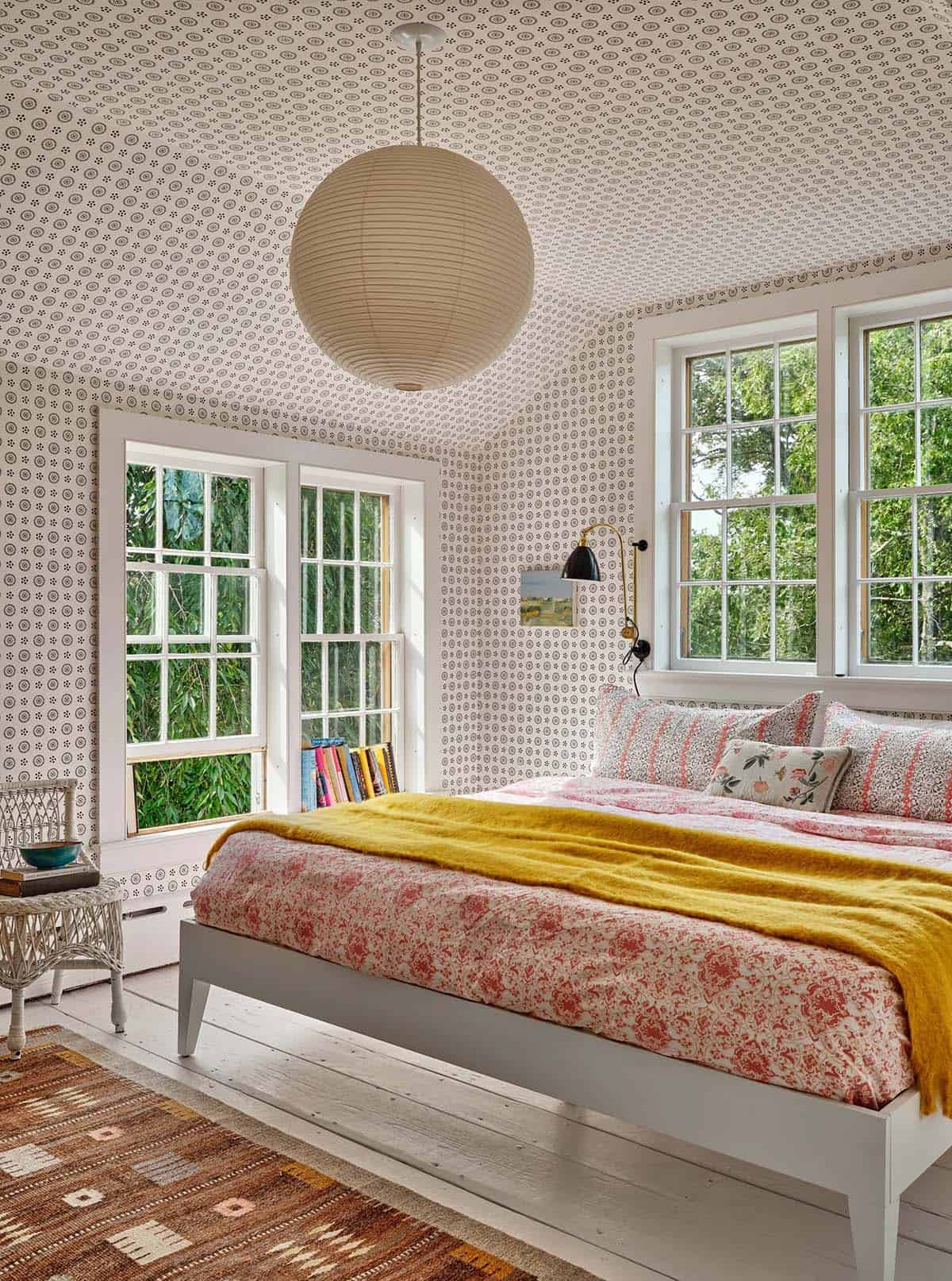 Attic bedroom with all-over patterned wallpaper, paper lantern pendant, yellow throw, and garden views