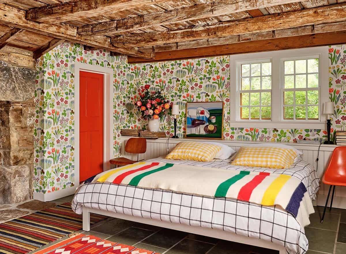 Guest bedroom with bold floral wallpaper, striped Hudson Bay blanket, and red door