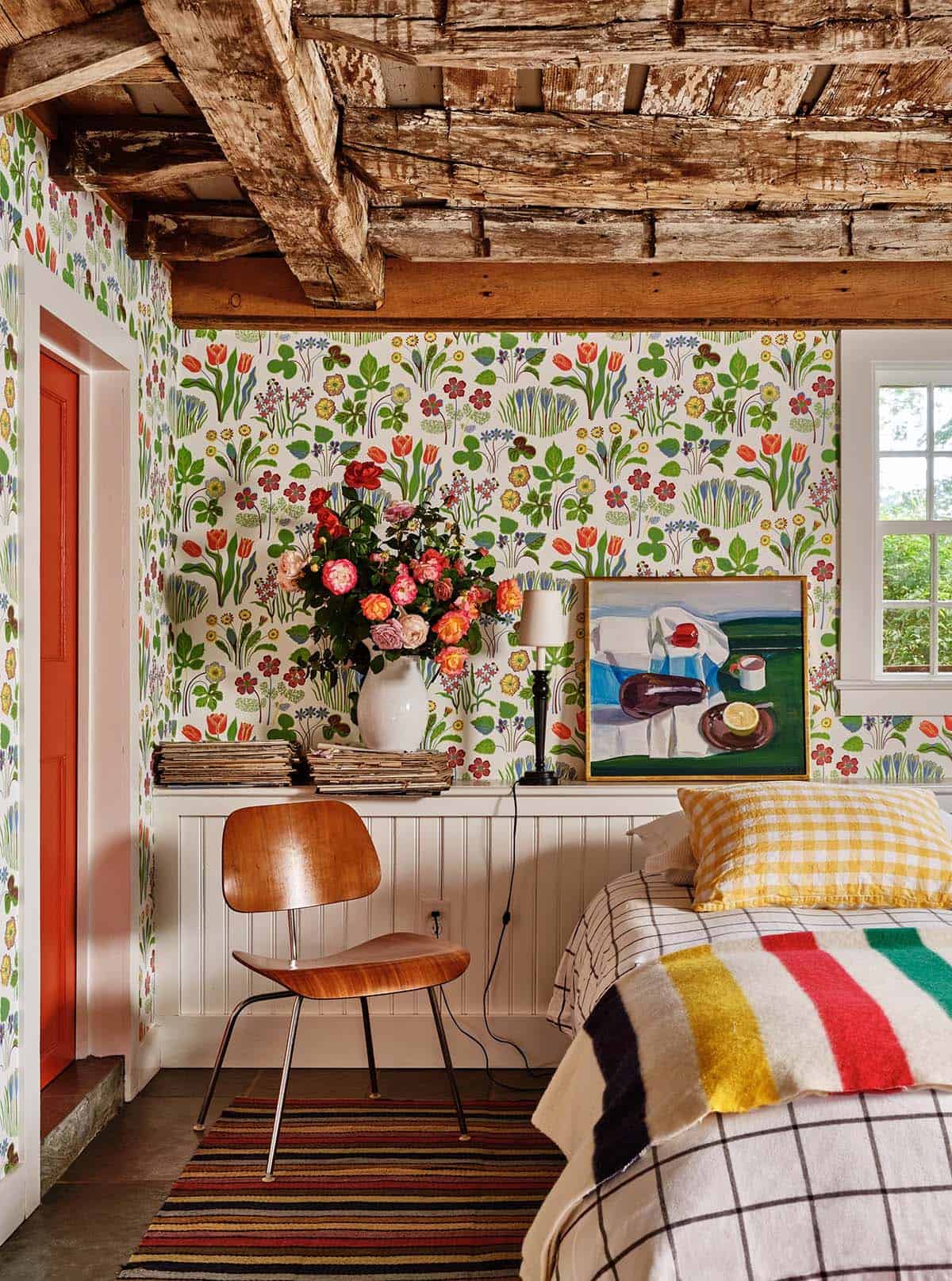Bedroom with vibrant floral wallpaper, Eames chair, vintage art, and exposed timber ceiling
