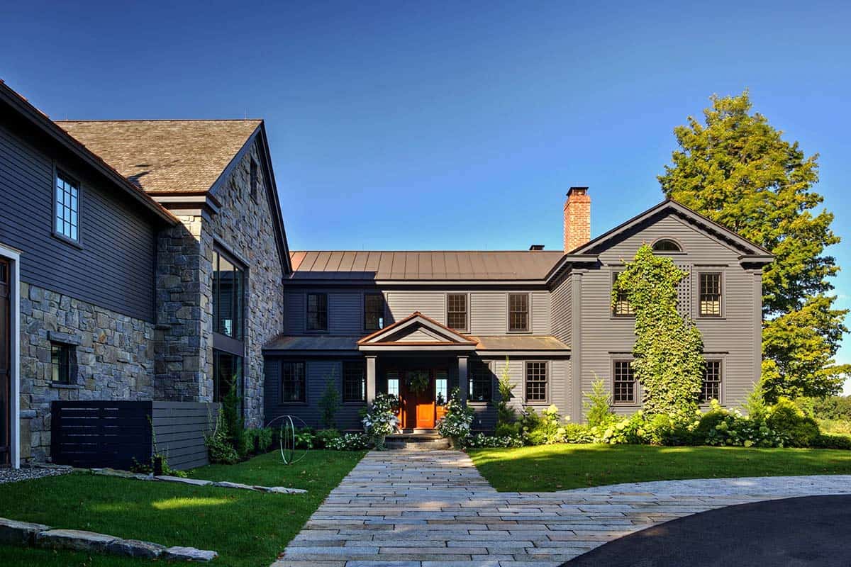 Historic farmhouse restoration with dark gray siding, stone addition, and warm wood entry door in New York