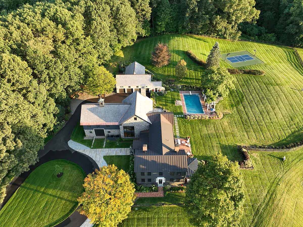 Aerial view of historic farmhouse estate with pool, pickleball court, and lush grounds in New York