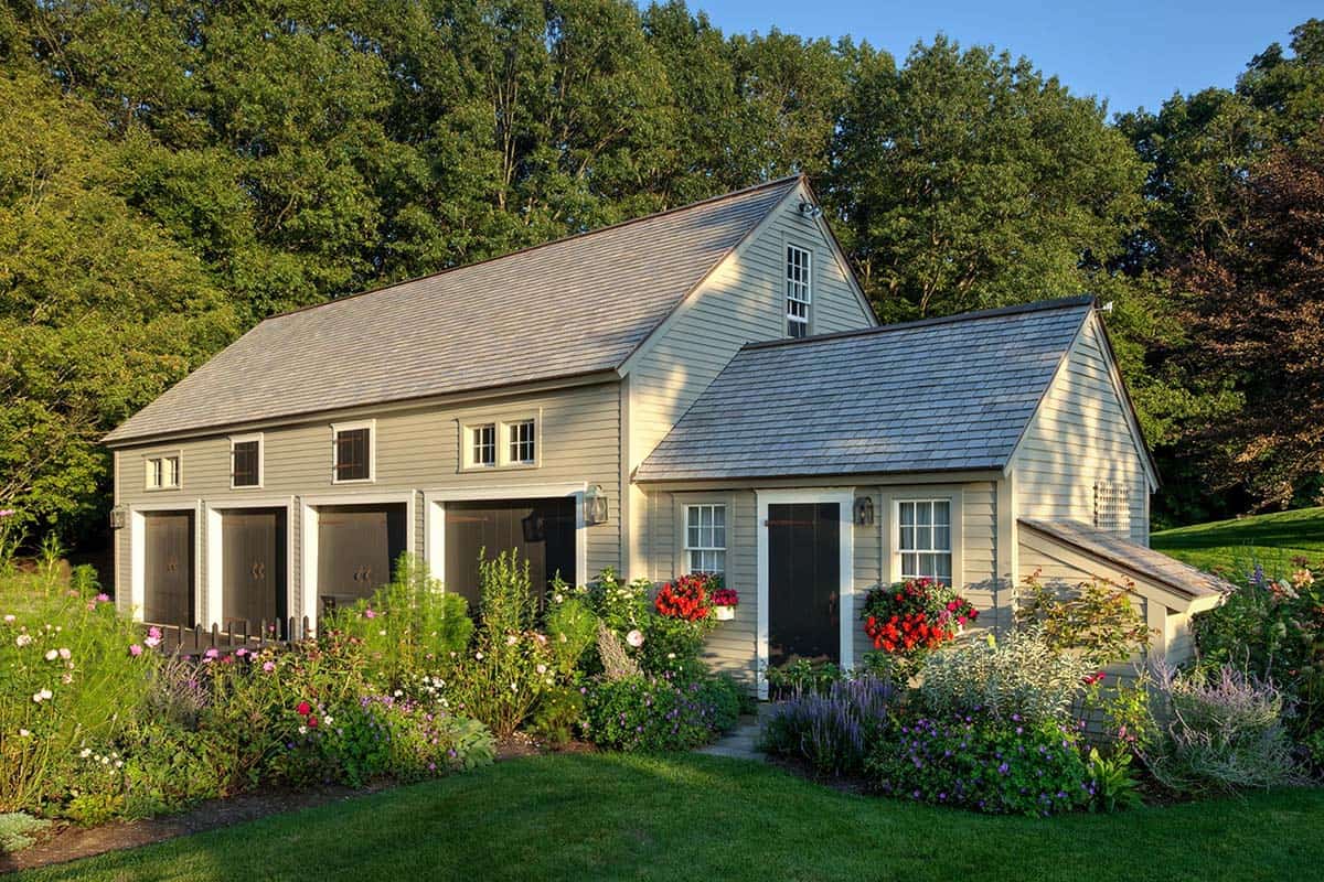 Charming carriage house with cream siding, flower boxes, and cottage gardens in full bloom
