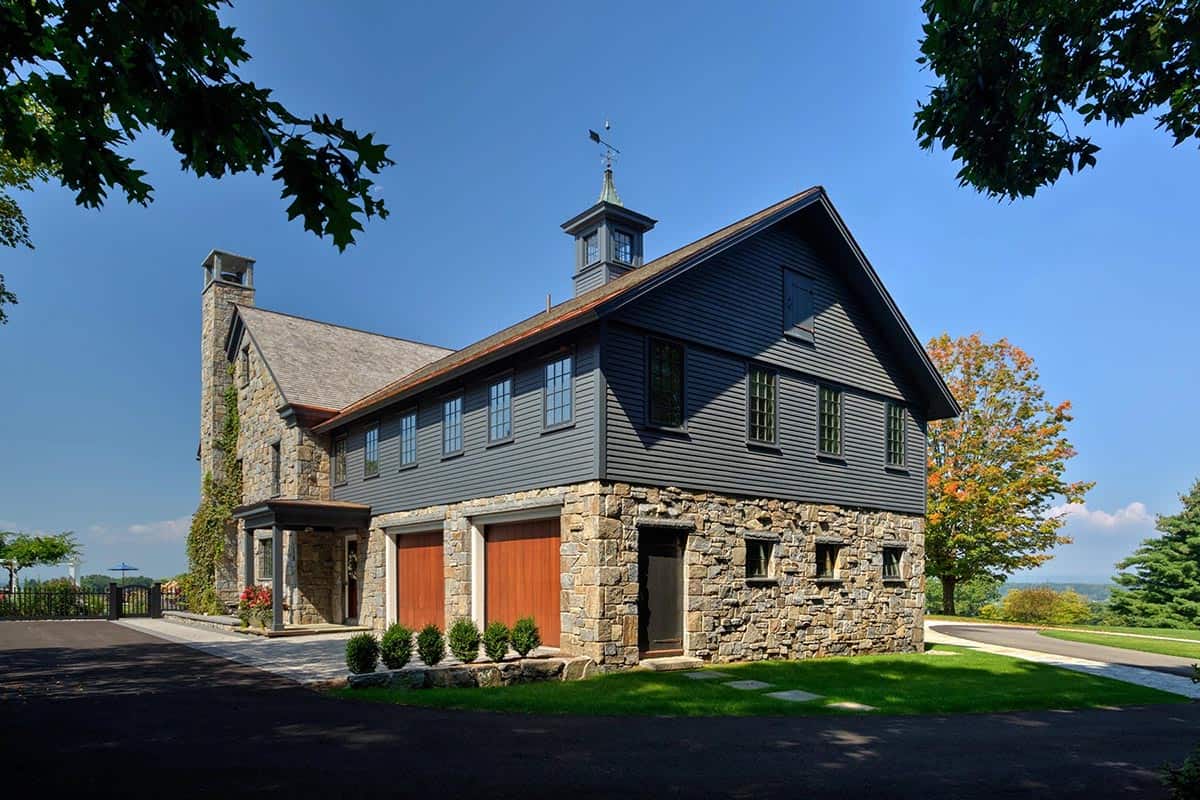 Stone and dark siding barn with cupola, weather vane, copper roof accents, and wood garage doors