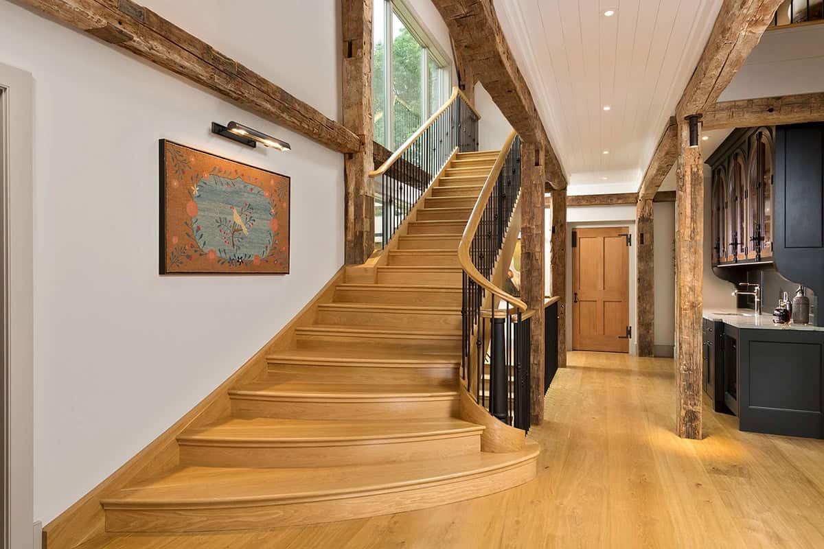 Curved oak staircase with iron balustrade, reclaimed timber beams, and wide plank hardwood floors