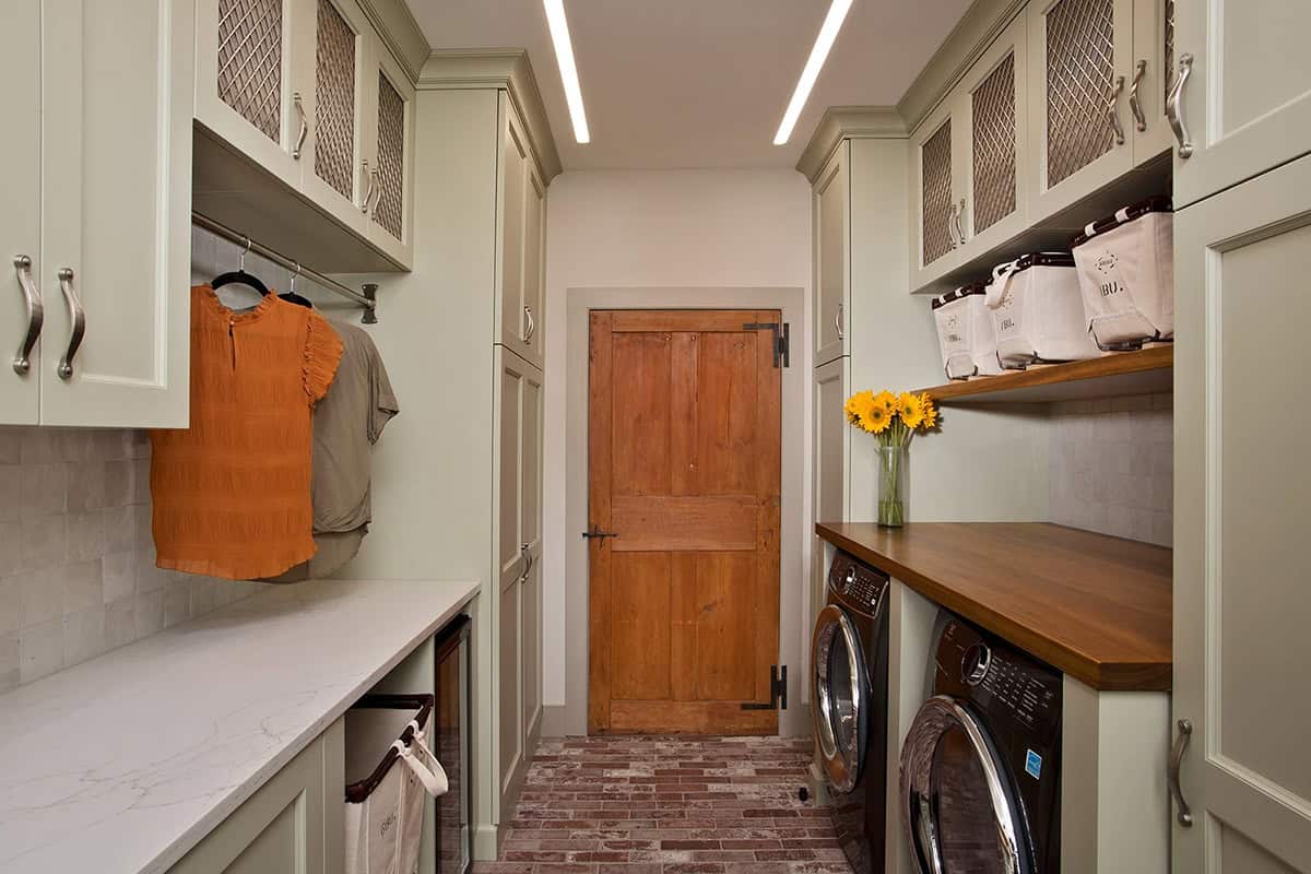 Laundry room with sage green cabinetry, butcher block countertop, brick floor, and original barn door