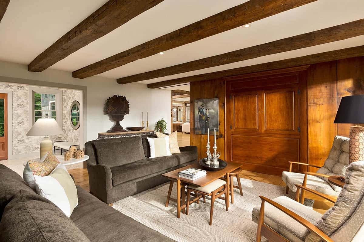 Cozy sitting room with exposed ceiling beams, charcoal sofa, wood paneling, and toile wallpaper alcove