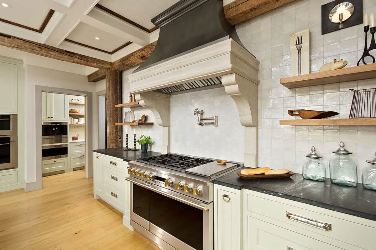 Kitchen range wall with stone hood surround, hexagonal tile backsplash, professional range, and open wood shelving
